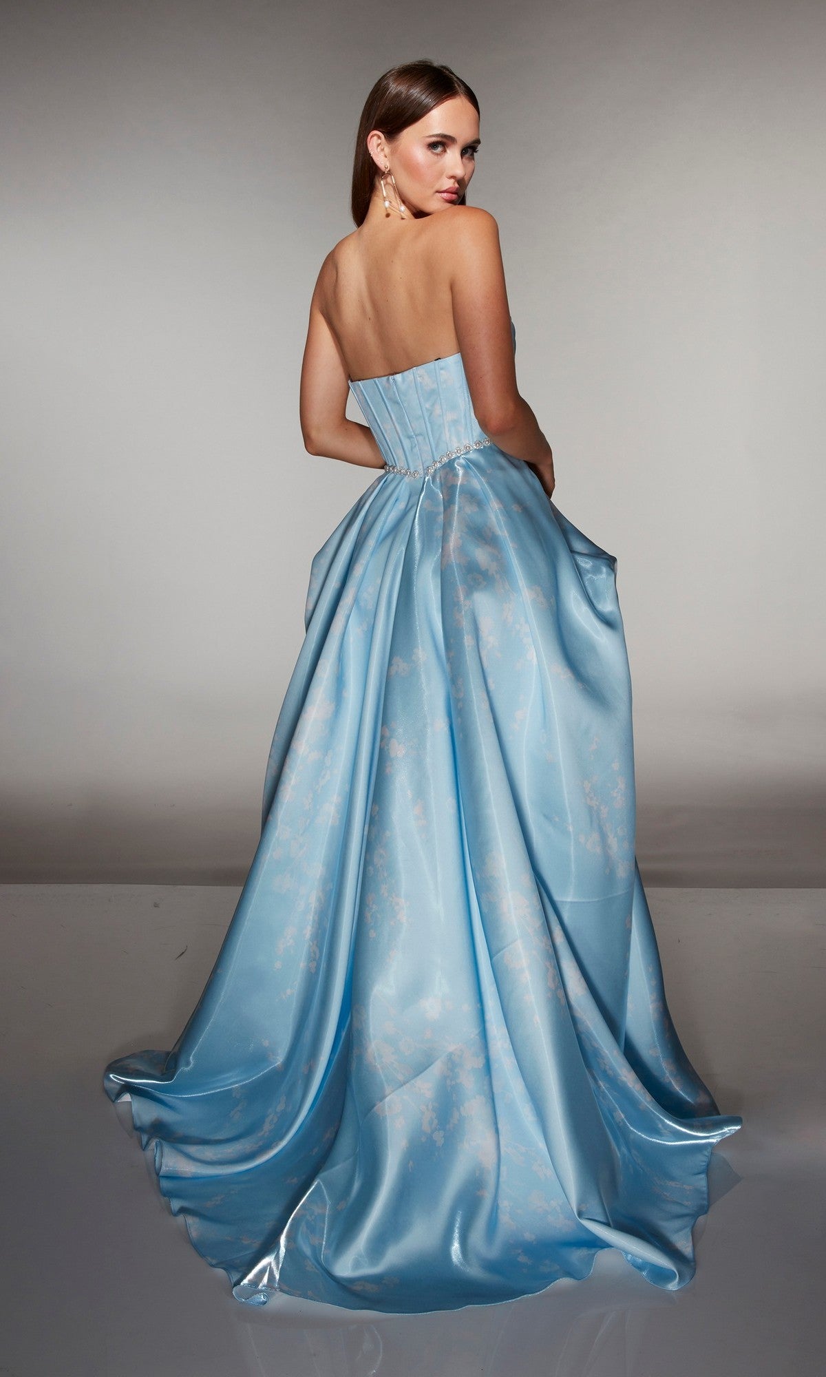 A woman stands facing away, looking over her shoulder against a plain background, wearing the Alyce 61989 Long Prom Dress featuring a strapless satin ball gown silhouette with a corset bodice.